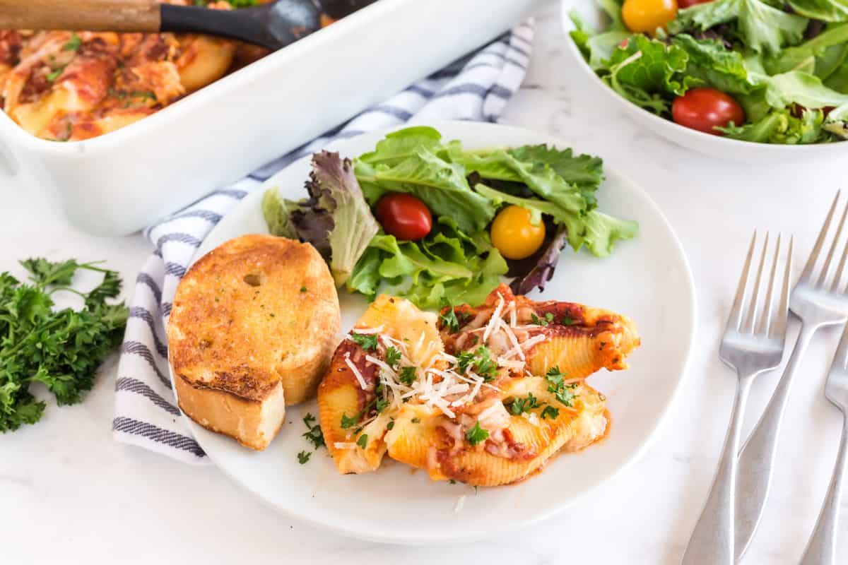 stuffed shells on a white plate with salad and garlic bread