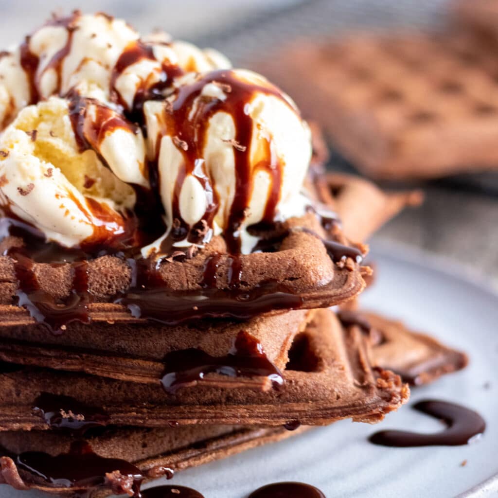 square pic of chocolate waffles topped with vanilla icecream and chocolate syrup