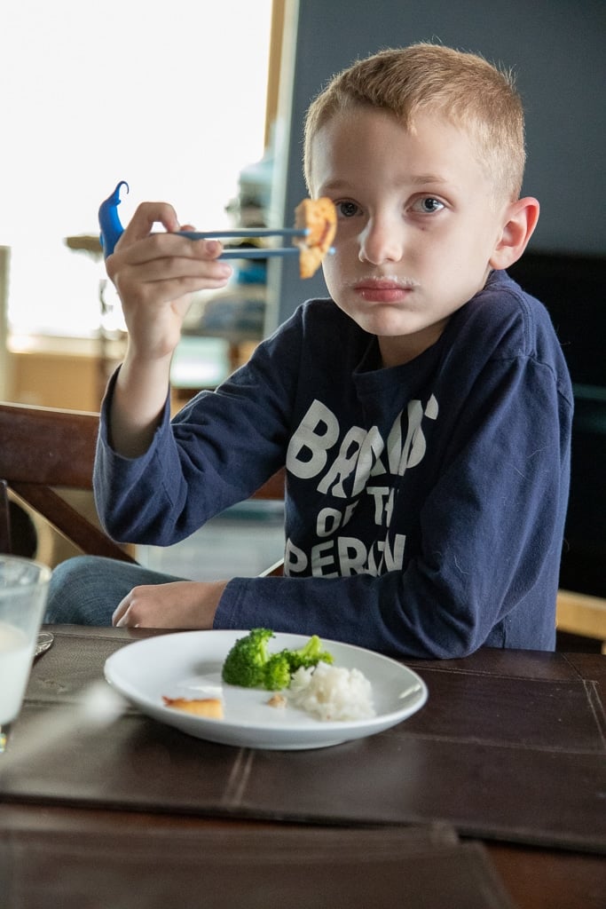 boy with blue chopsticks eating stir fry.