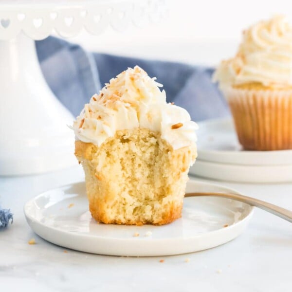 coconut cupcake on a white plate, cut open to show texture