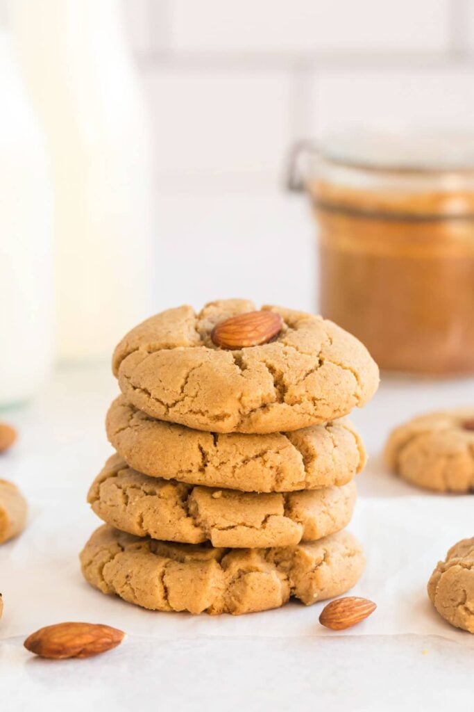 almond butter cookies stacked with almonds, milk and a jar of almond butter