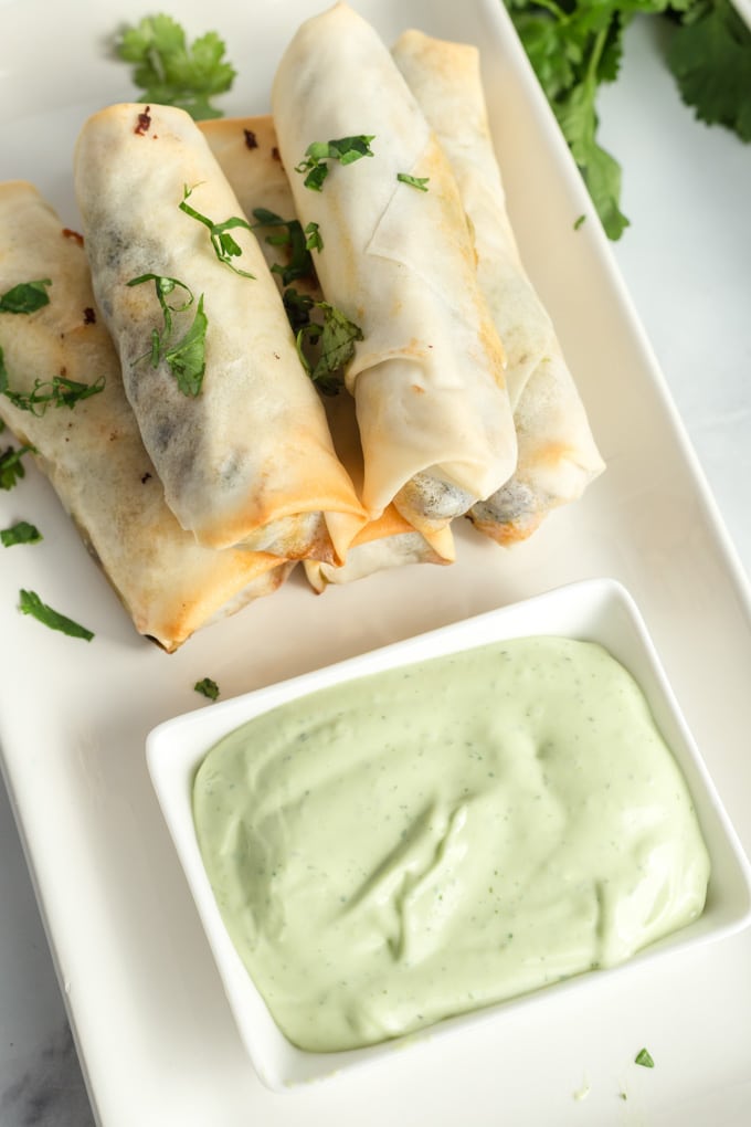 egg rolls on a white platter with avocado dipping sauce