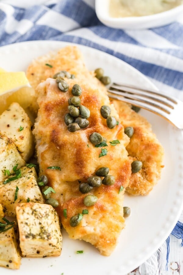 chicken piccata on a plate with capers and a blue and white napkin