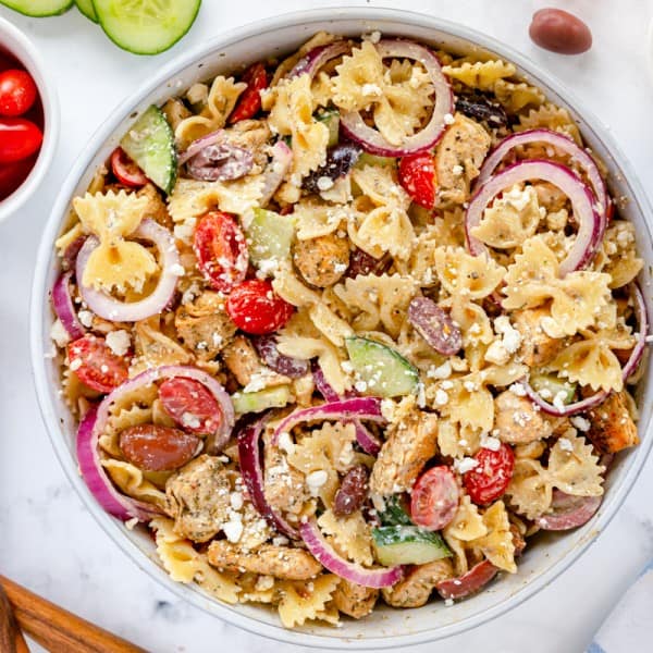greek pasta salad with wooden serving spoons and veggies