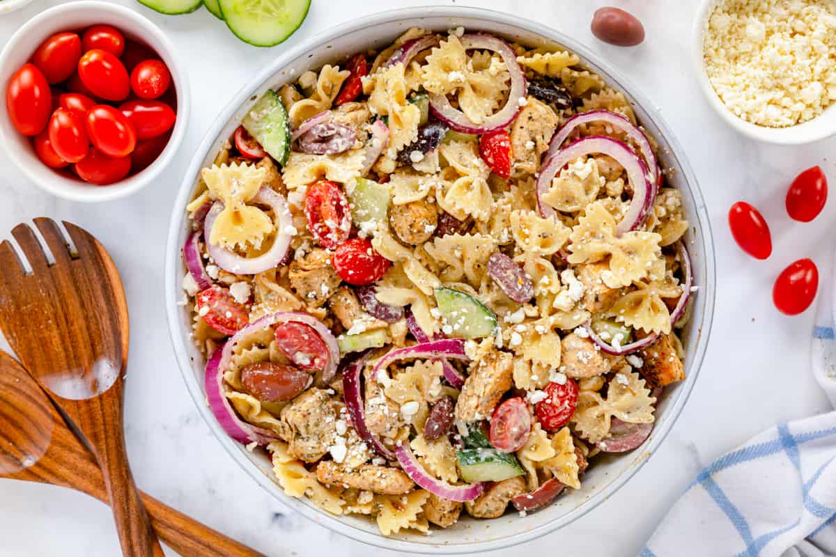 greek pasta salad with wooden serving spoons and veggies