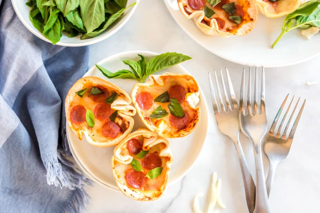 3 tortilla pizzas with basil on a plate.