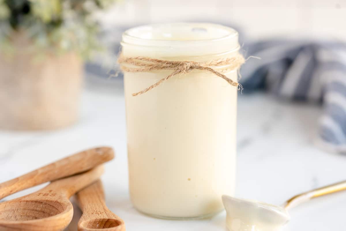 A jar of condensed milk next to a wooden spoon.