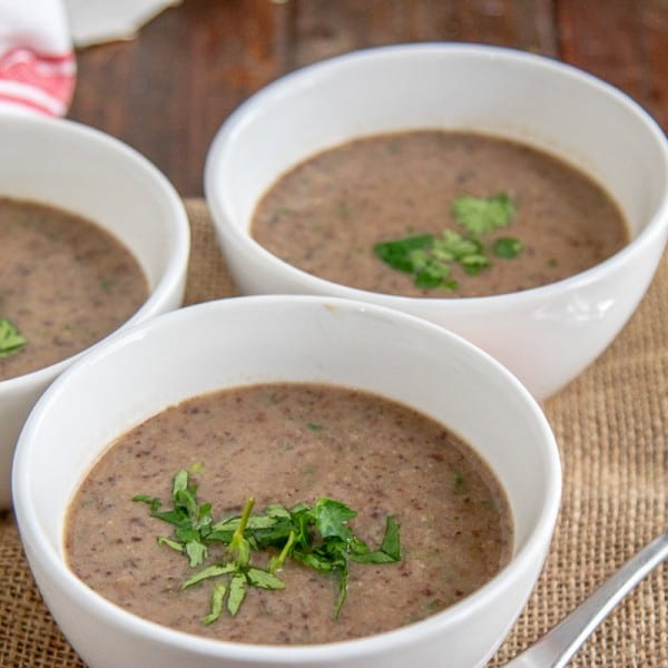 3 bowls of black bean soup on a table with a spoon