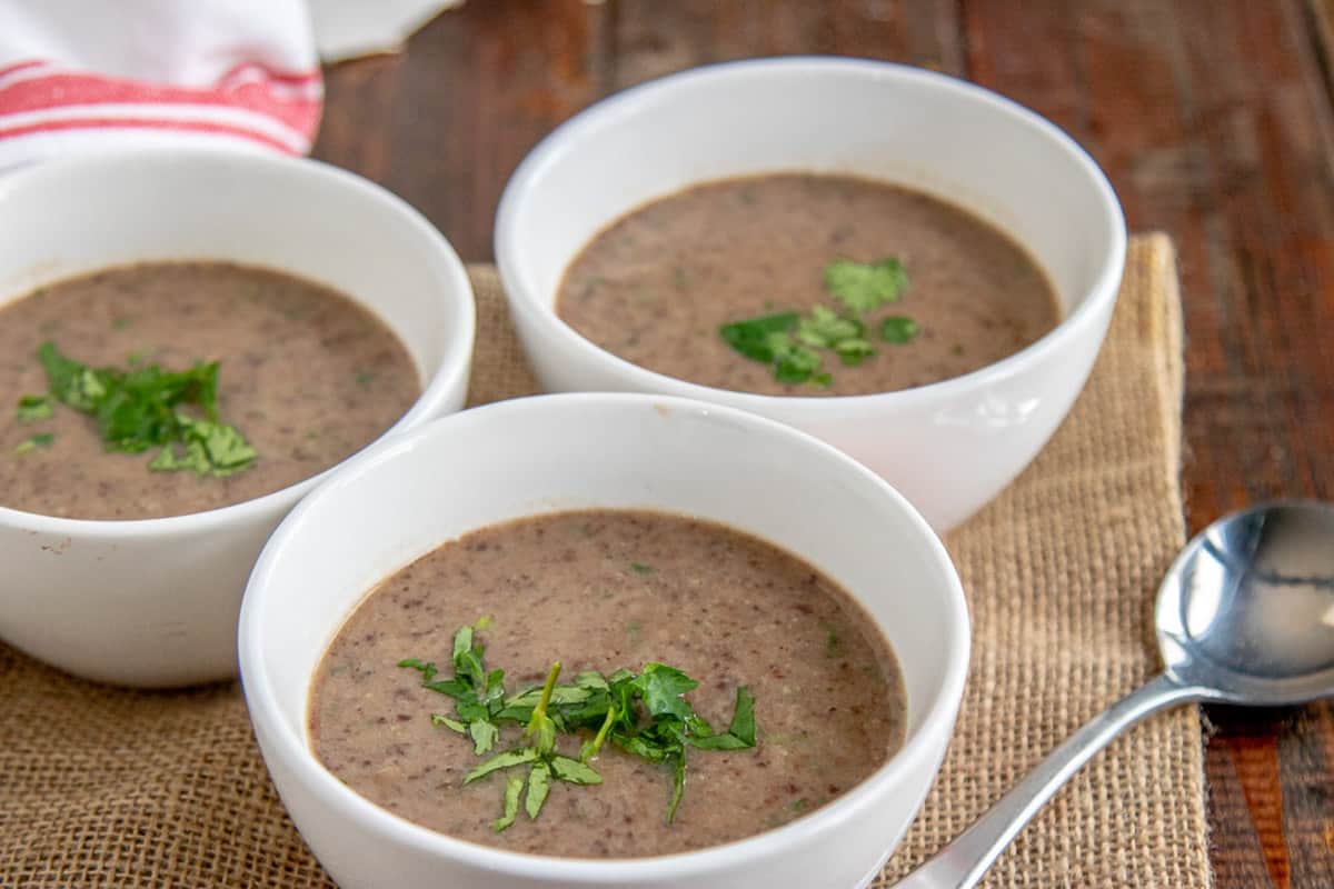 3 bowls of black bean soup on a table with a spoon