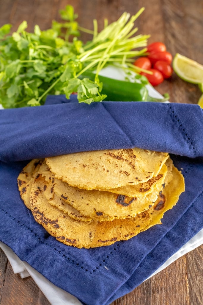 Homemade Corn Tortillas in a blue napkin with cilantro, limes and tomatoes
