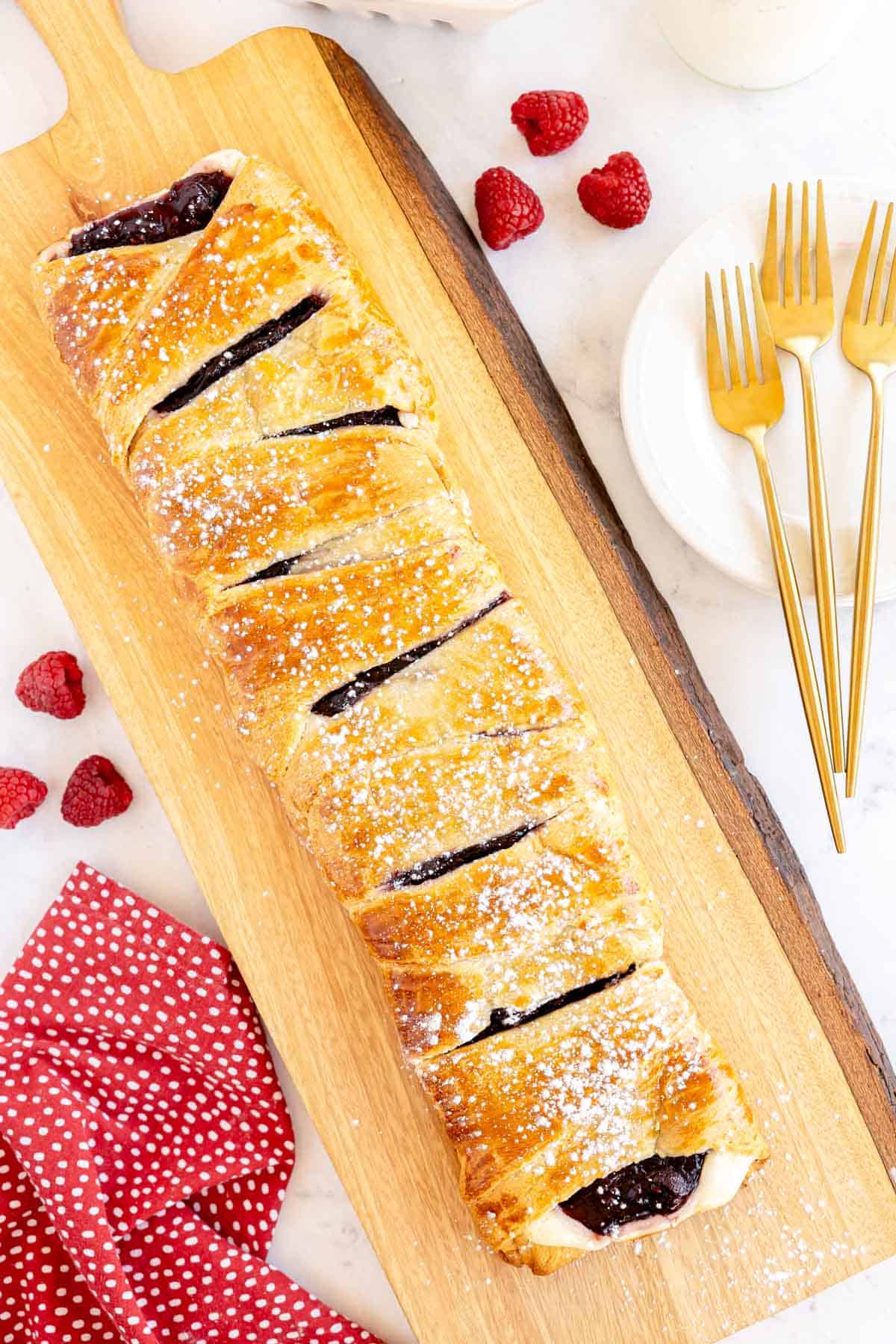 A raspberry-filled danish topped with powdered sugar on a cutting board.