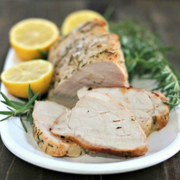 pork tenderloin slices on a white plate with lemons and rosemary