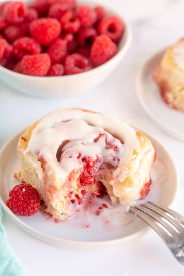 raspberry sweet roll on a plate with bowl of raspberries
