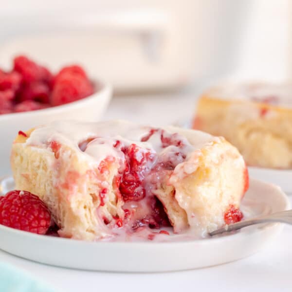 raspberry sweet roll on a plate with bowl of raspberries
