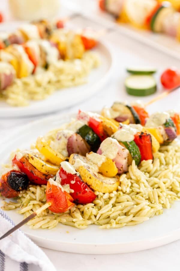 vegetable skewers on a bed of orzo on a white plate
