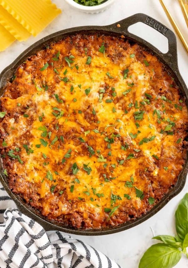 skillet lasagna on a wooden board with white plates, silverware and parsley