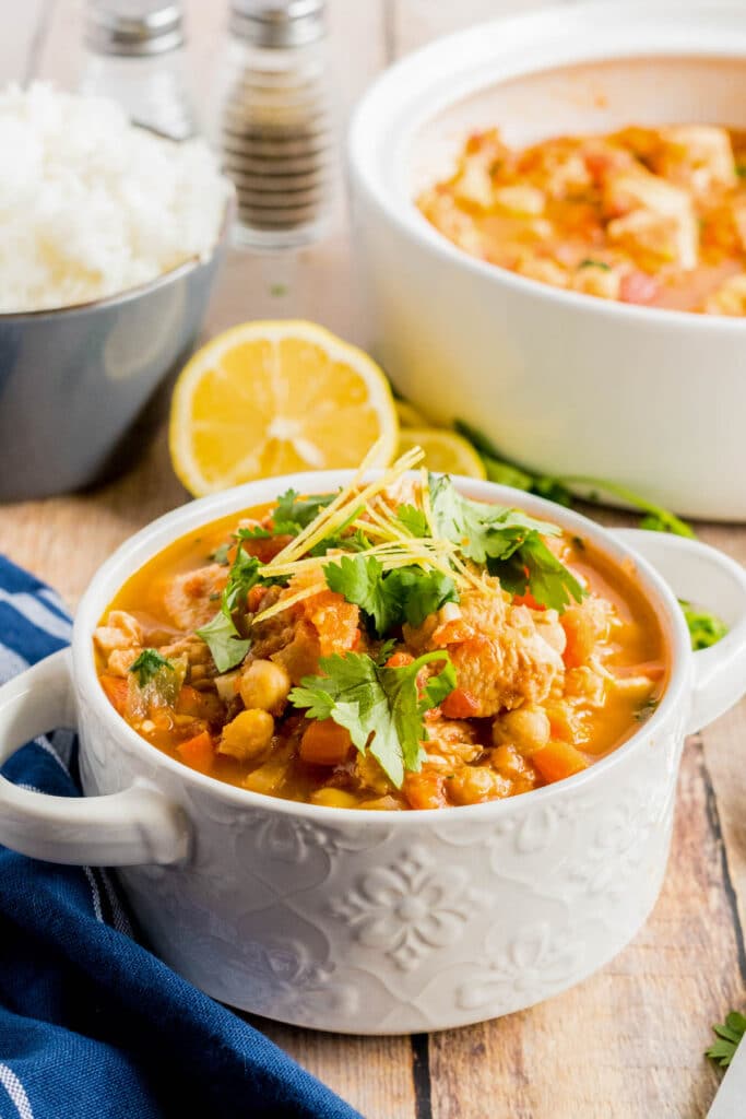 chicken stew in a white bowl with lemon and cilantro