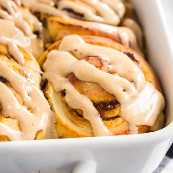 pumpkin cinnamon rolls with frosting in a white casserole