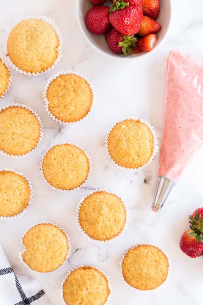 vanilla cupcakes with a piping bag and strawberries