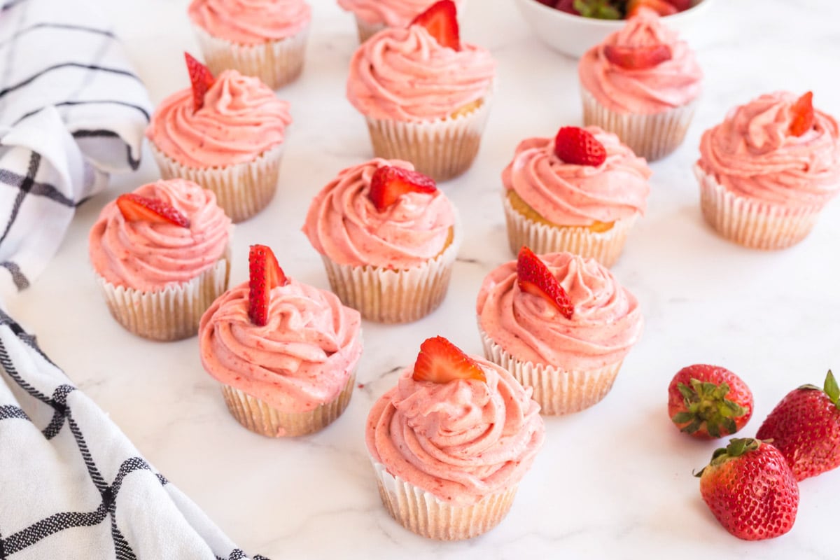 vanilla cupcakes with strawberries on a white board
