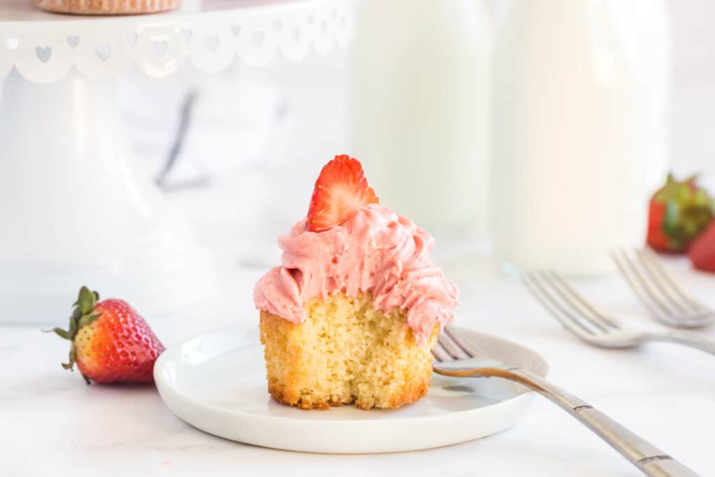 vanilla cupcake cut in half on a white plate with a strawberry