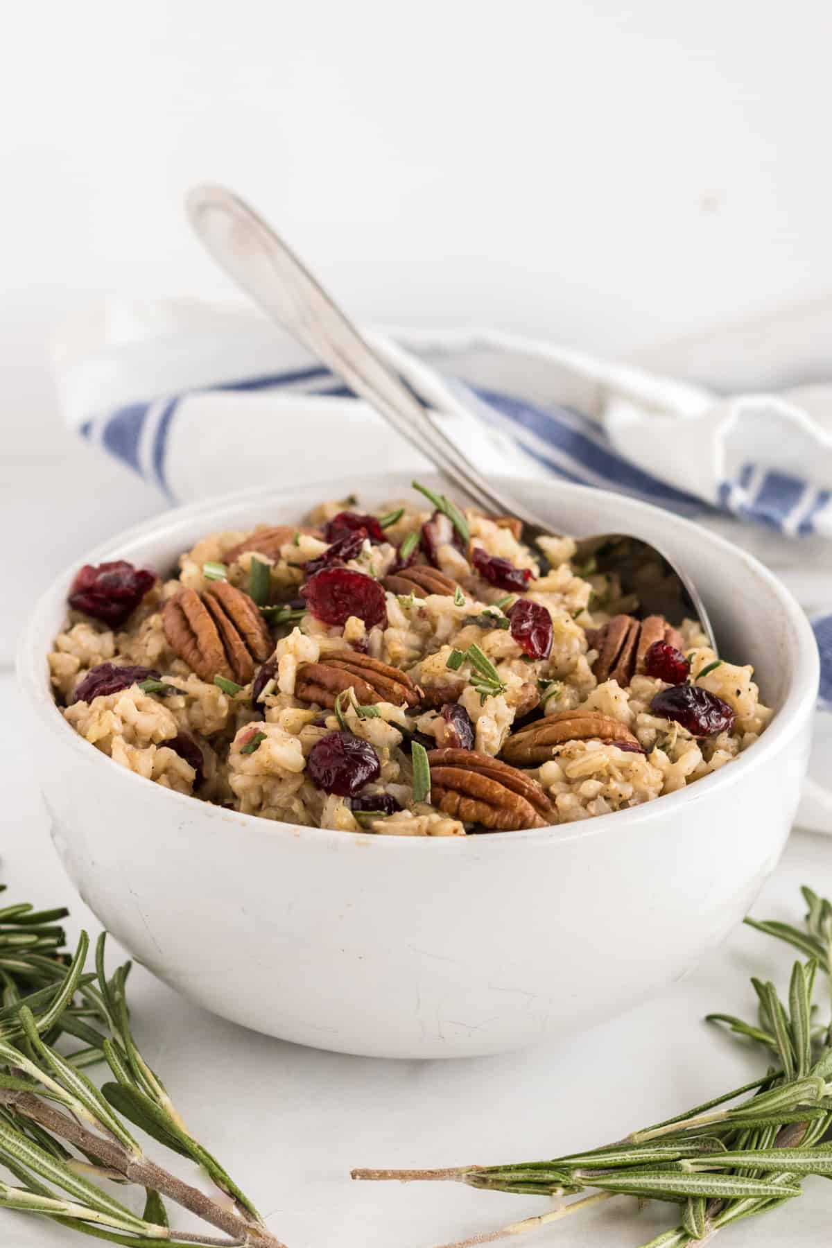 brown rice pilaf in a white bowl with rosemary, pecans and cranberries