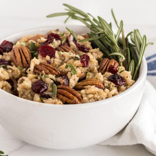 brown rice pilaf in a white bowl with rosemary, pecans and cranberries