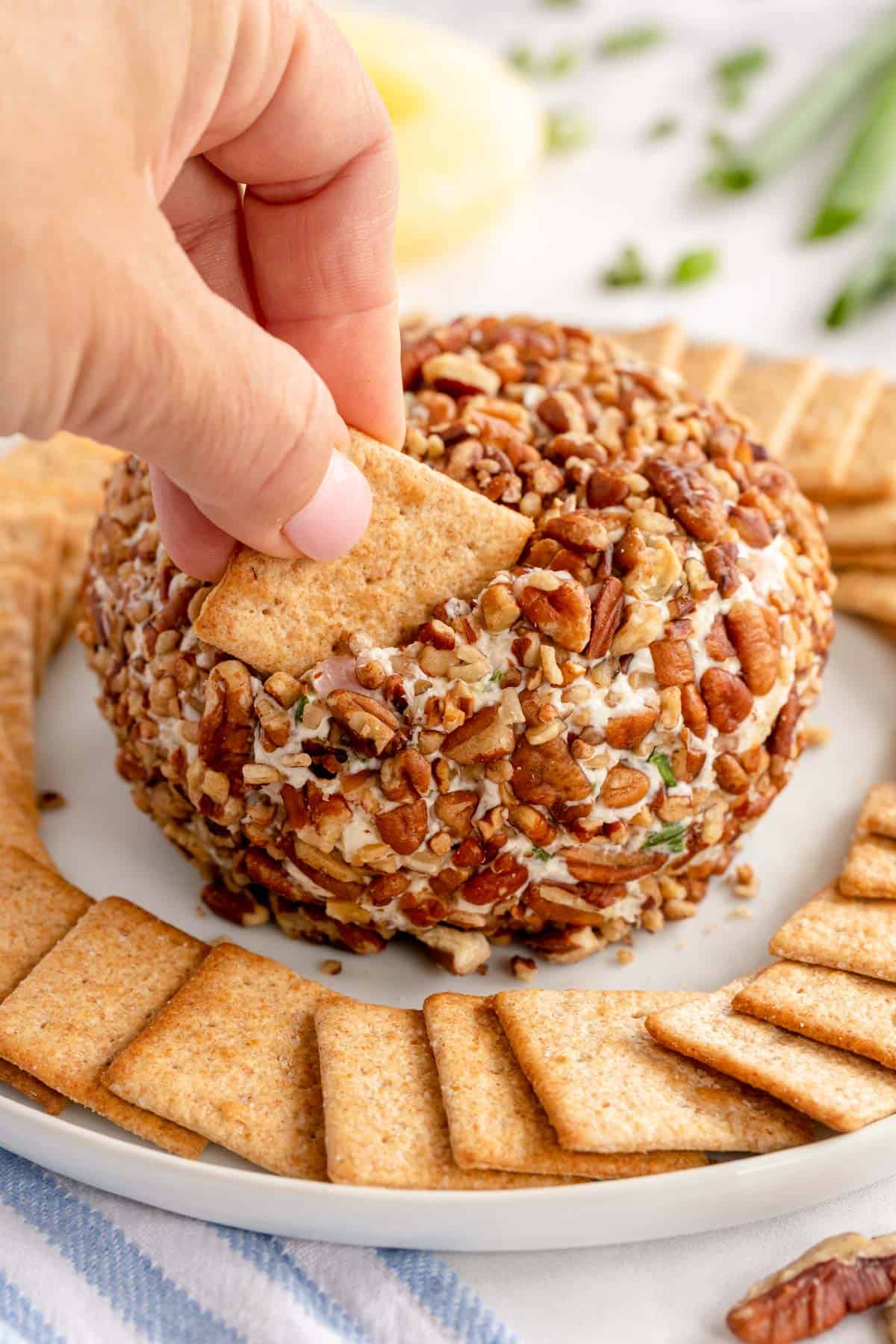 a hand digging into a pineapple cheese ball with a cracker