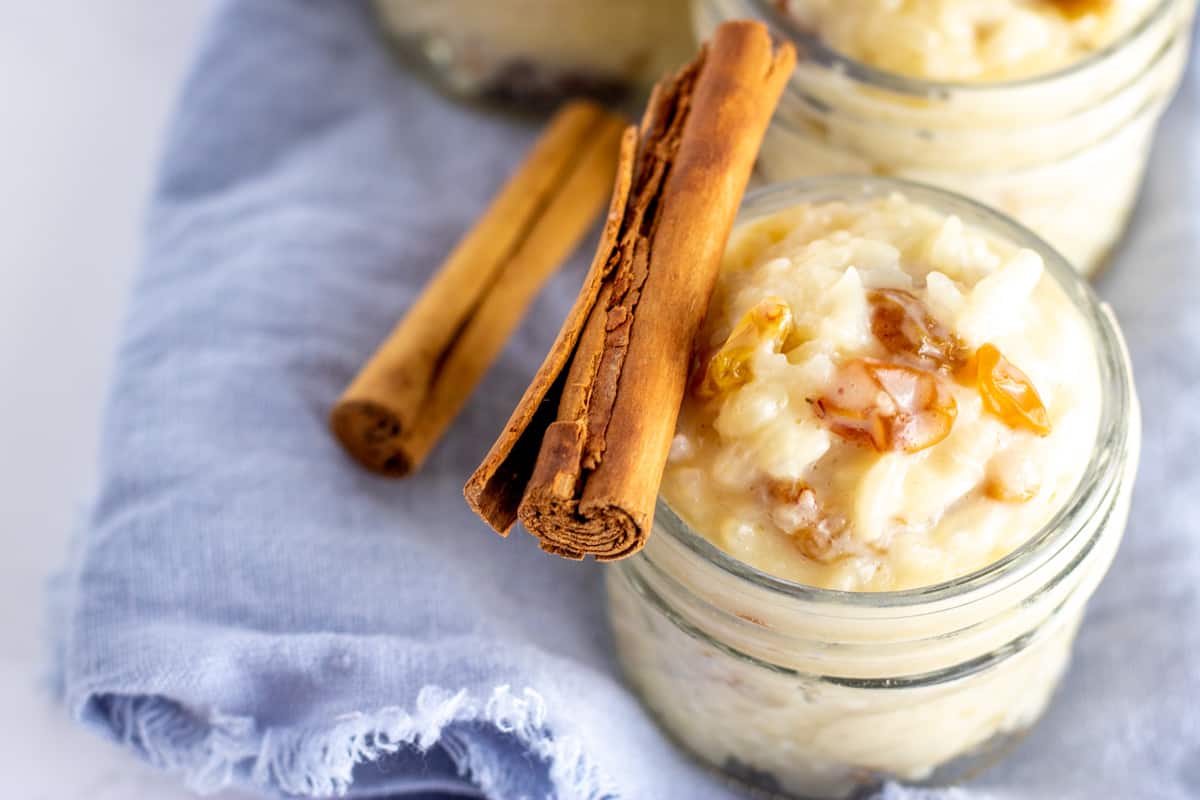 rice pudding in glass jars with cinnamon sticks laid across the top