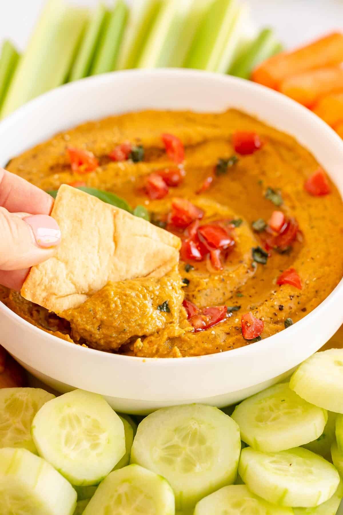 Tomato Basil Hummus in a bowl with a pita chip