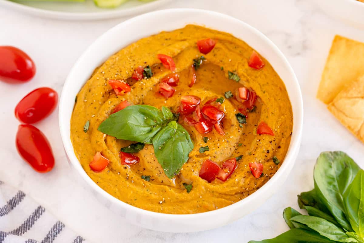 Tomato Basil Hummus in a bowl with dippers surrounding