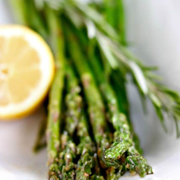 asparagus with lemon and rosemary in a white dish.