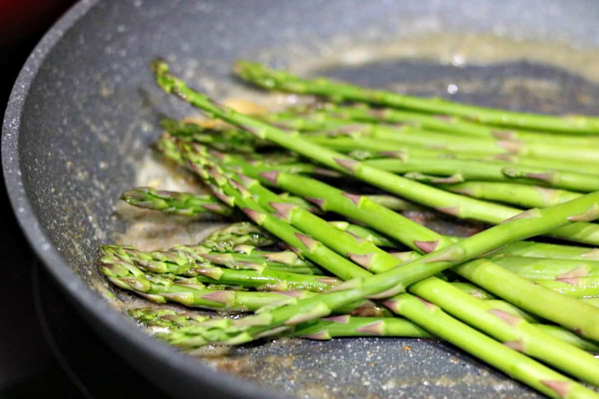 a skillet with raw asparagus in it.