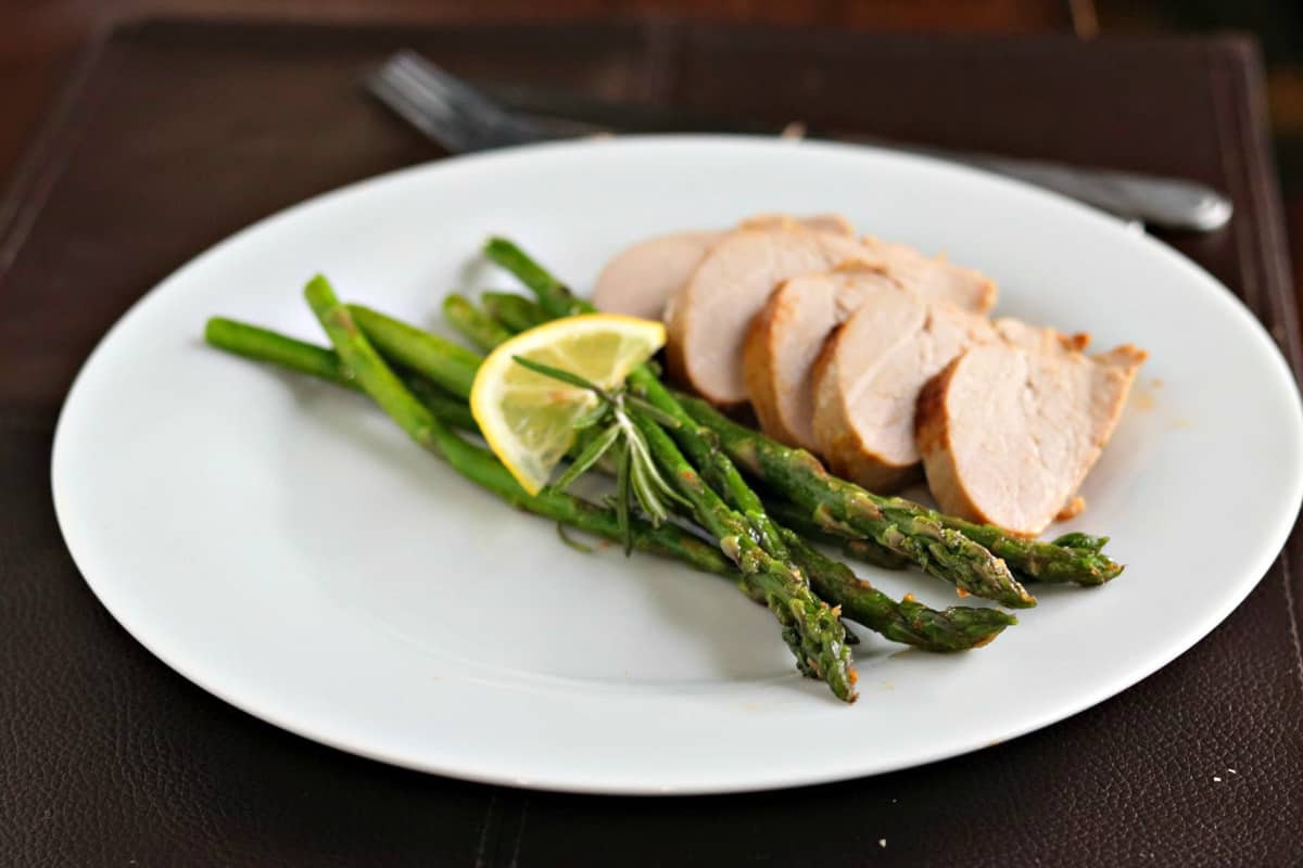asparagus on a plate with sliced pork tenderloin and a wedge of lemon.