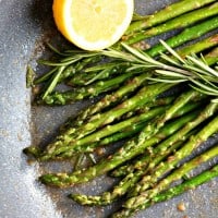 a skillet with cooked asparagus in it with lemon and rosemary.