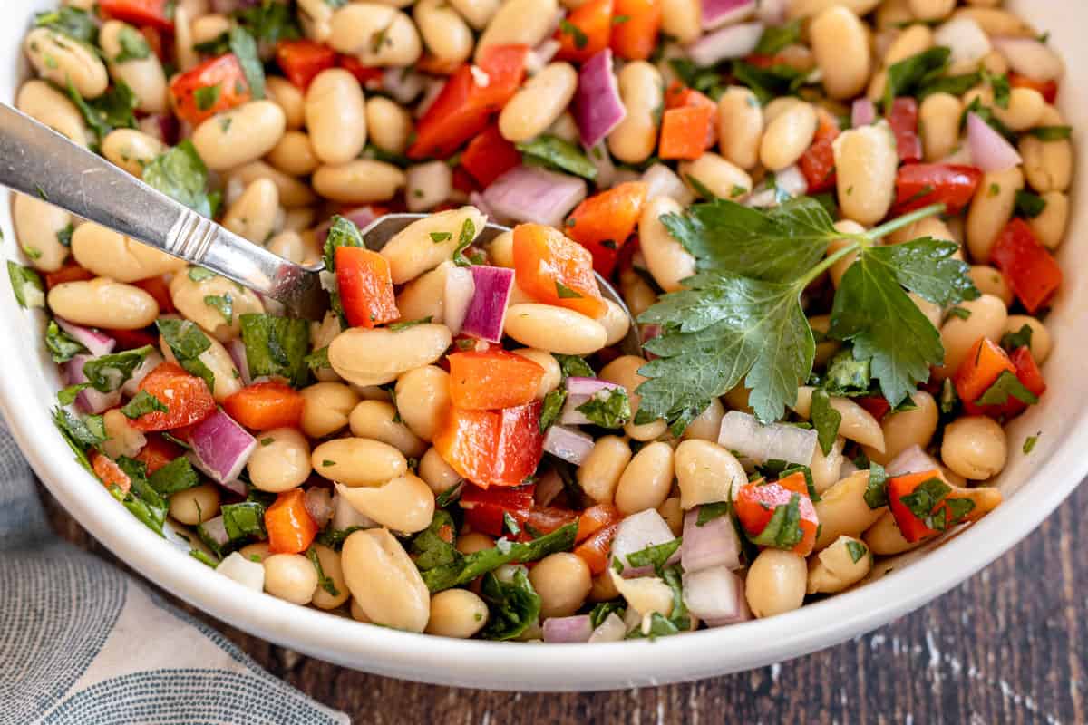 white bean salad in a white bowl on a wood background.