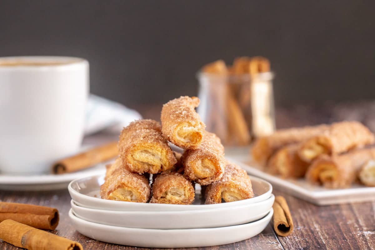 cinnamon cream cheese roll ups on a white plate with a coffee cup