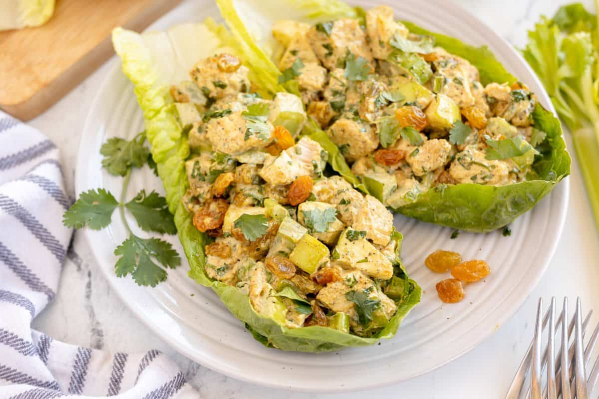 curried chicken salad served in lettuce cups on a white plate.
