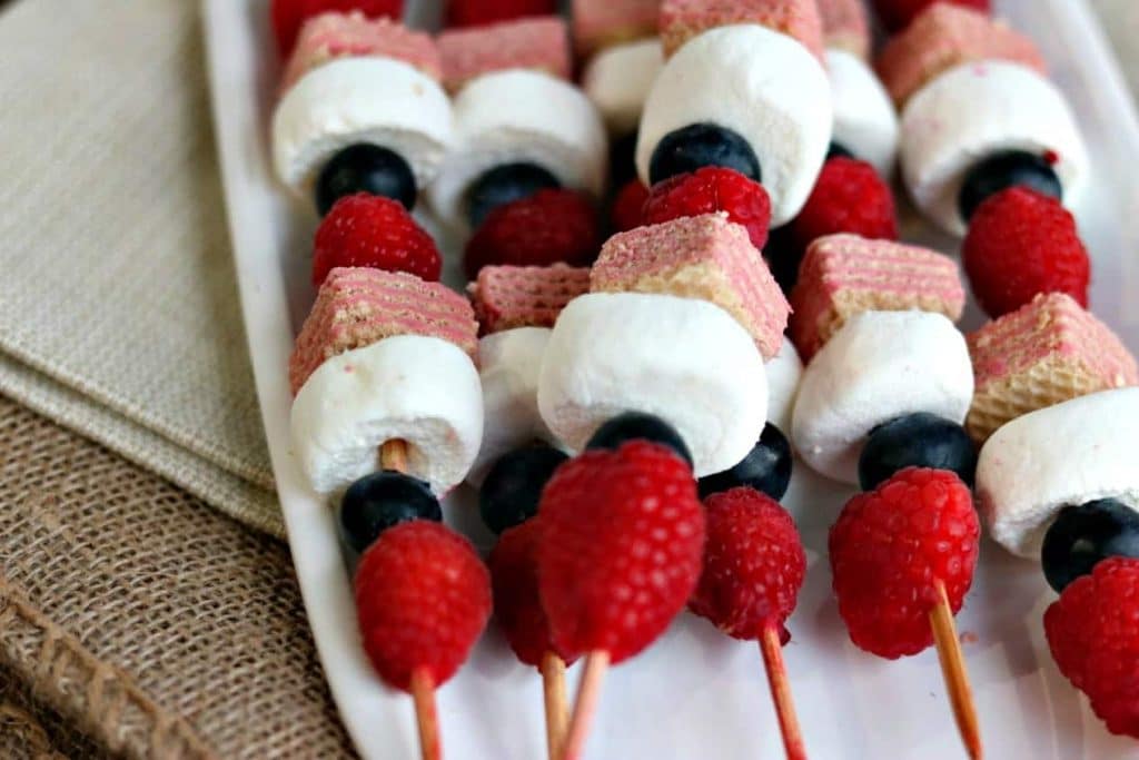 red white and blue fruit and cookie kabobs on a white plate 