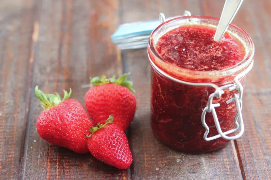 Canning Recipes Post: a jar of strawberry jam next to three strawberries