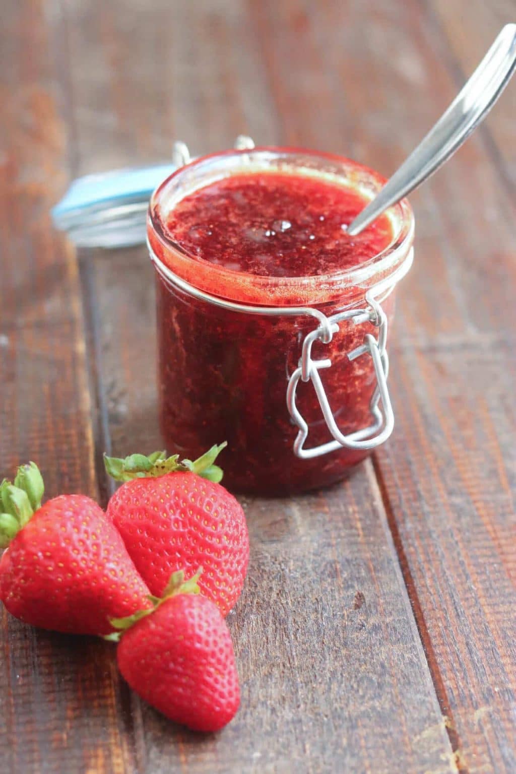 jar of strawberry jam with a spoon in it with strawberries alongside it