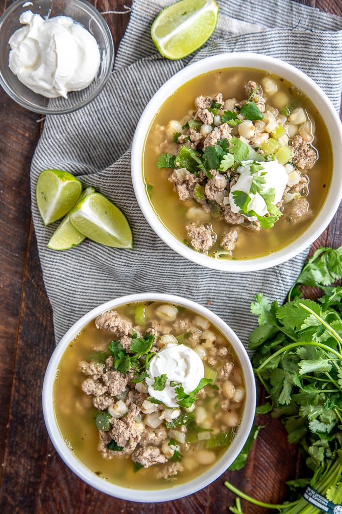 turkey chili in two white bowls with limes, sour cream and cilantro
