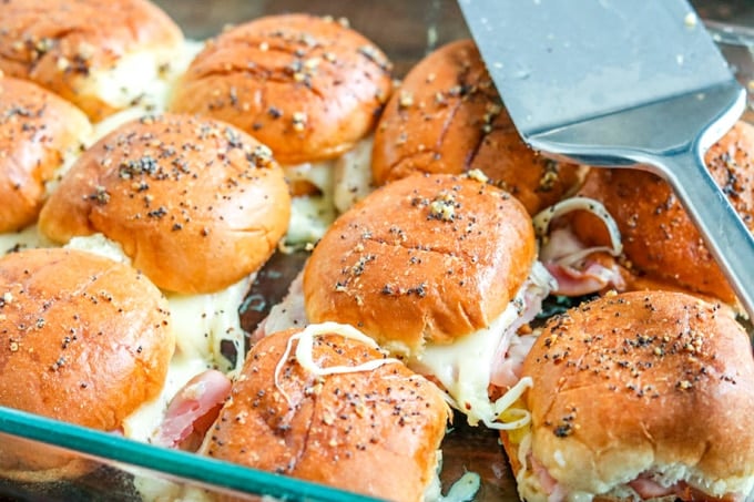 Closeup of ham and pineapple sliders in glass baking dish with spatula laying on top.