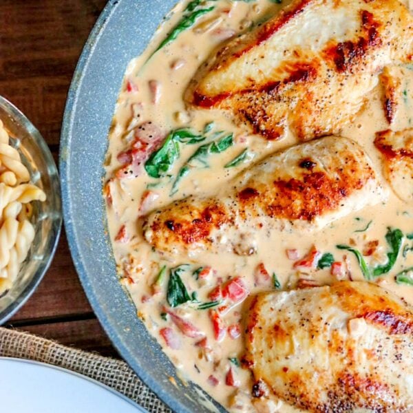 chicken in a creamy sauce in a skillet with a bowl of pasta off to the side