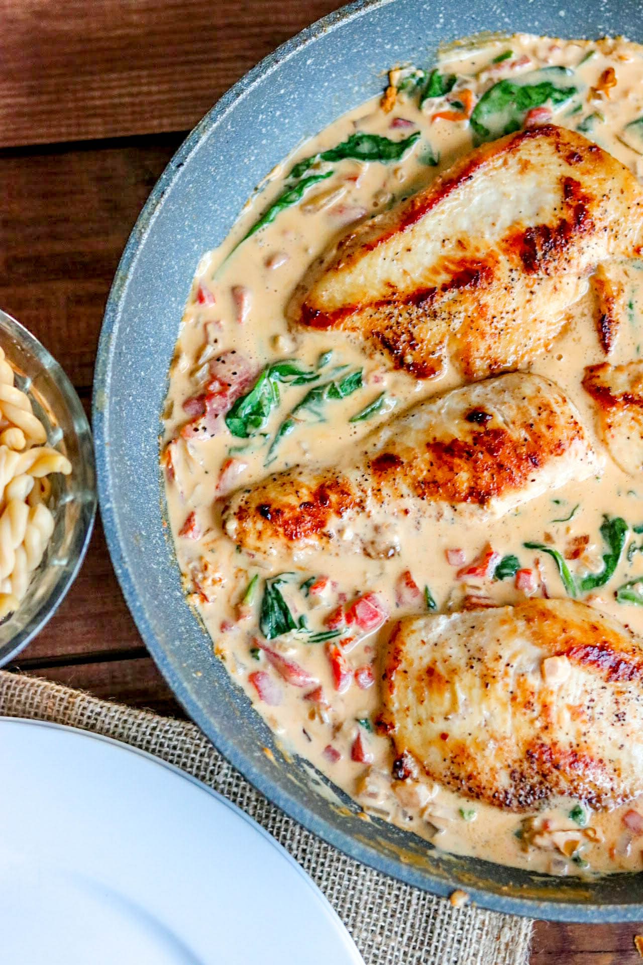 chicken in a creamy sauce in a skillet with a bowl of pasta off to the side