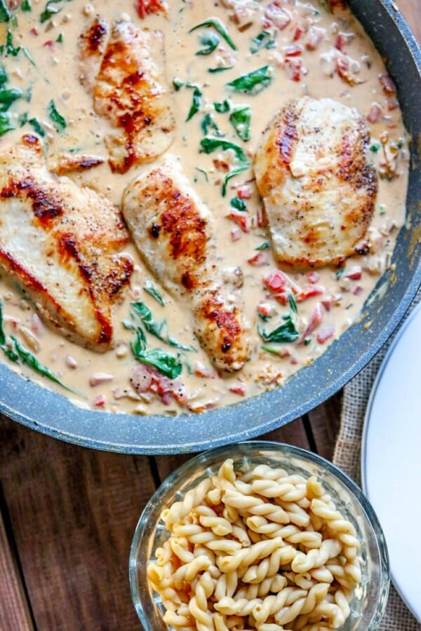 creamy mediterranean chicken in a skillet with extra pasta in a bowl on the side