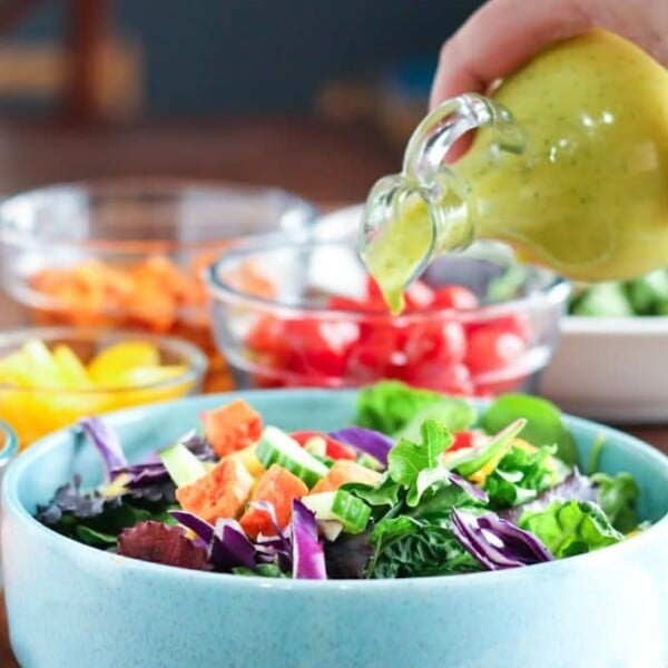mango salad dressing being poured on a salad from a glass cruet