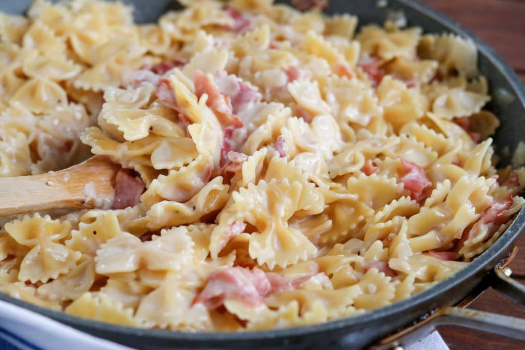 ham and cheese pasta with a wooden spoon in a skillet
