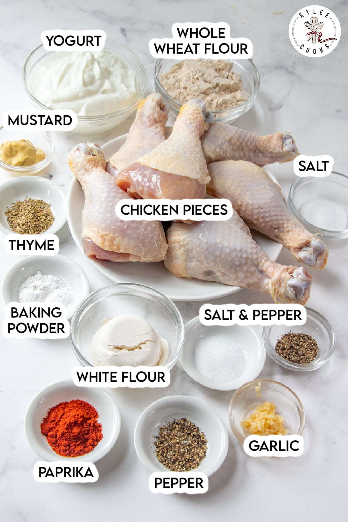 A plate of raw chicken pieces surrounded by small bowls of yogurt, whole wheat flour, white flour, baking powder, mustard, thyme, paprika, garlic, salt, and pepper&mdash;everything you need to make delicious oven fried chicken.