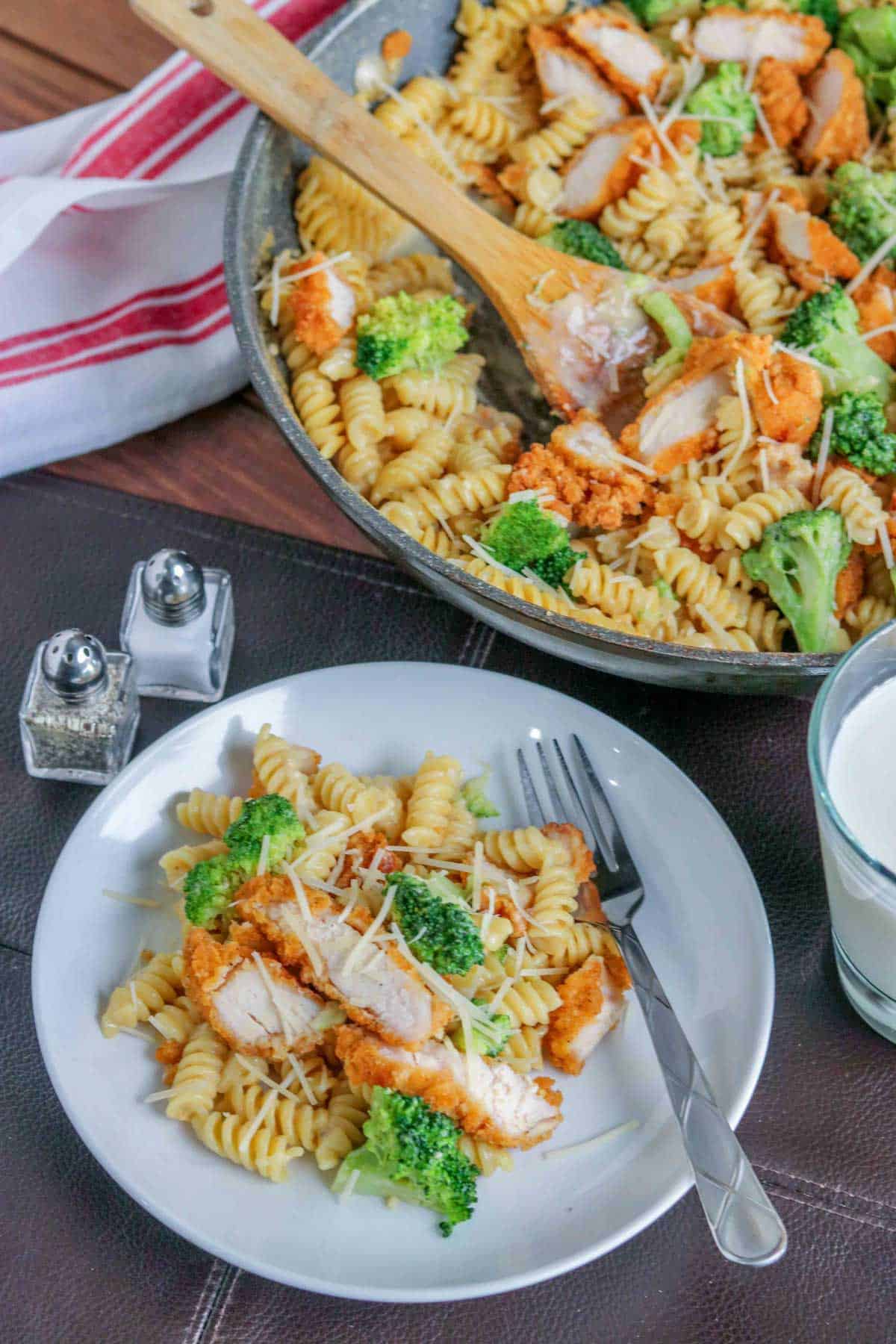 chicken and broccoli alfredo in a skillet, with a white bowl of pasta